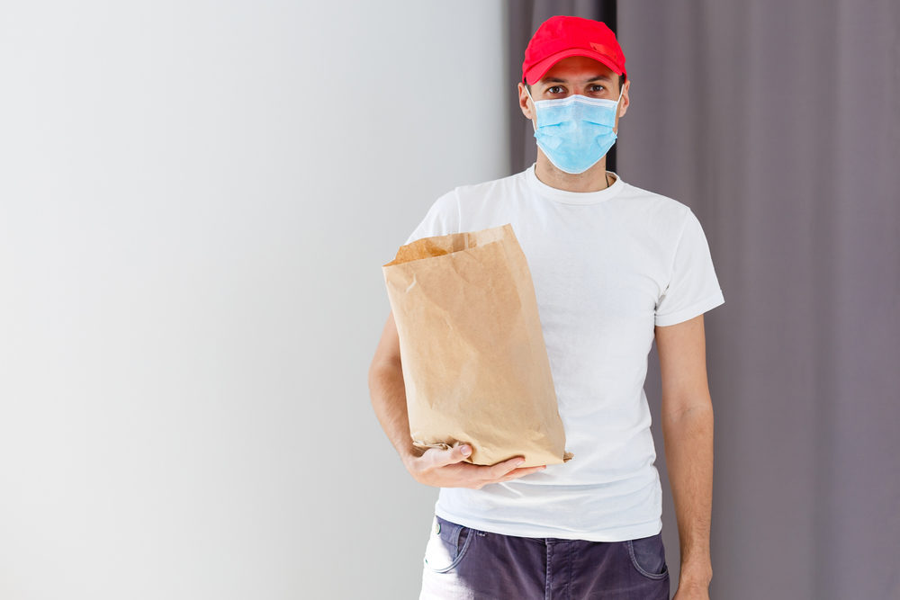 A facemask-wearing man holding a brown paper bag
