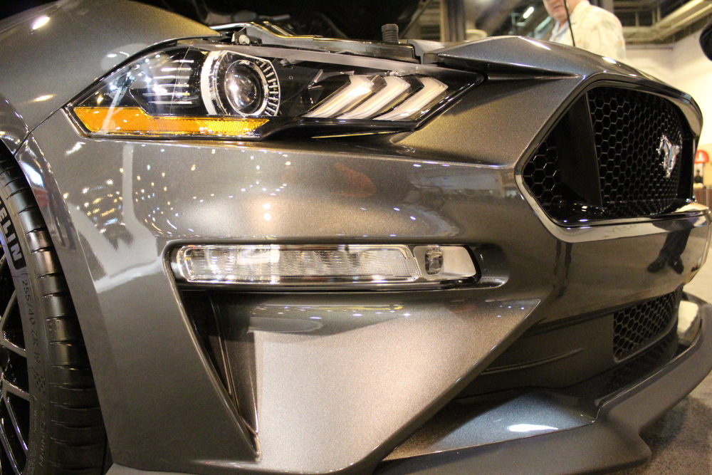 front view of a grey ford mustang with hood up being viewed by older man