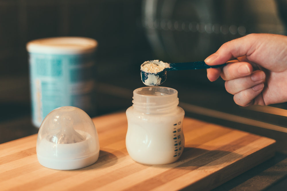 baby formula being prepared in a bottle on a cutting board with canister in background