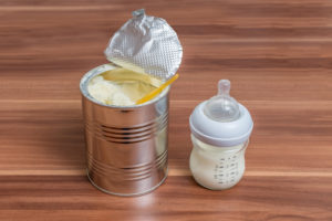 Powdered milk formula in can and bottle for feeding baby on wooden table.