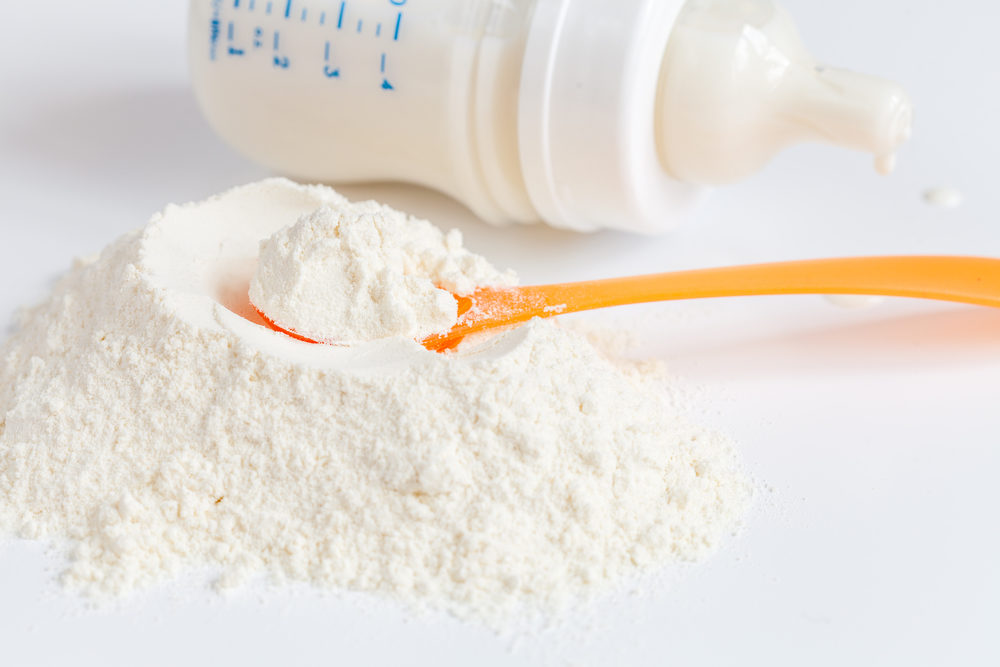 baby formula on a table with a scoop and a bottle in the background