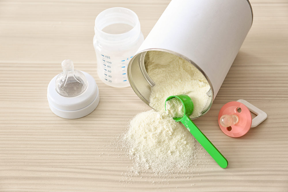 Feeding bottle with bank of baby milk formula on wooden background