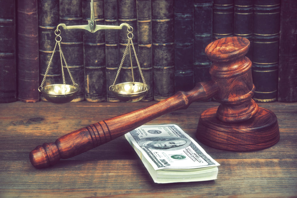 gavel and scales on desk with a stack of USD in front of books