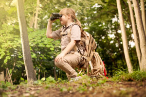 A young girl in a scout uniform looks through a pair of binoculars