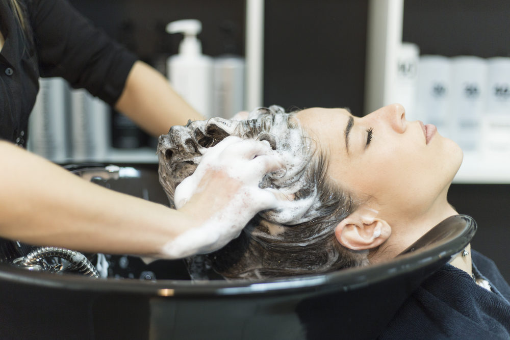 Beautiful young woman with hairdresser washing head at hair salon