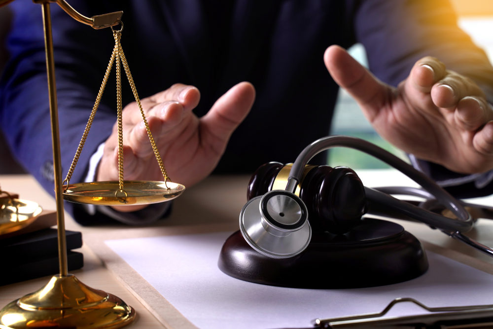 hands of an attorney at desk above gavel and stethoscope