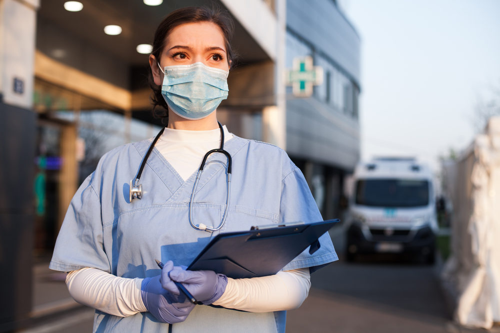 Young female EMS key worker doctor in front of healthcare ICU facility wearing protective PPE