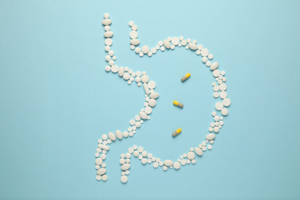 Pills laid out in the shape of a stomach on a blue background