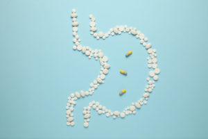 Pills laid out in the shape of a stomach on a blue background
