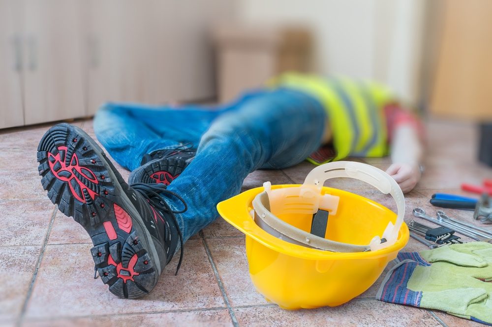 Construction worker laying on ground after injury with hard hat and gloves nearby