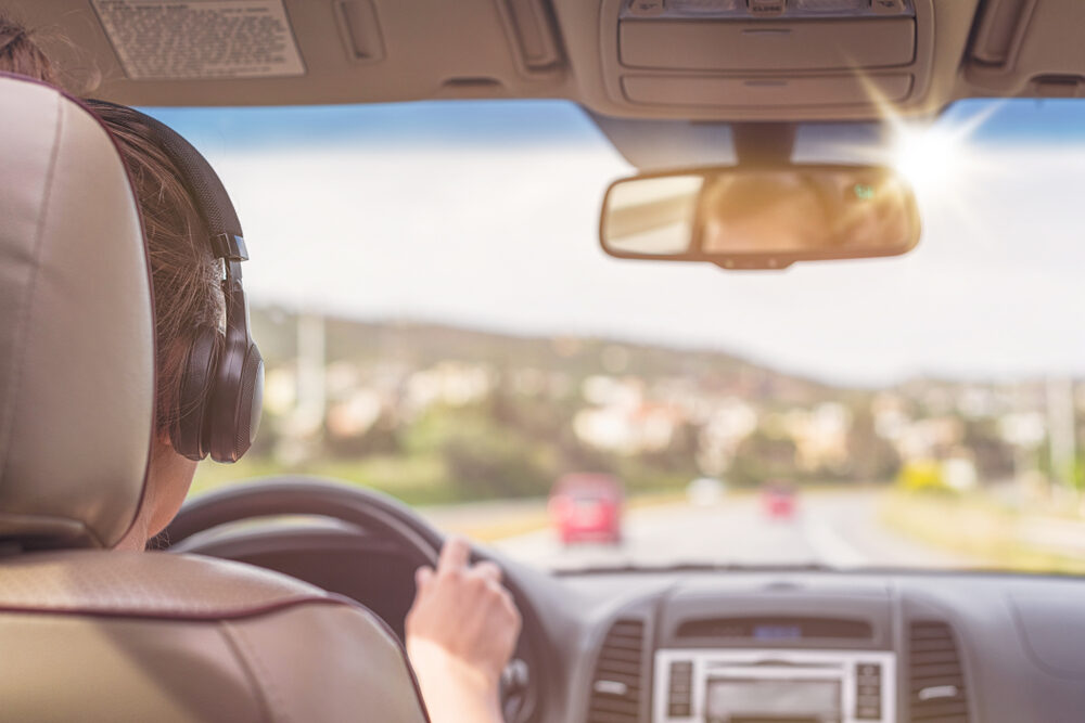 view from backseat of a female driver wearing headphones while driving on highway