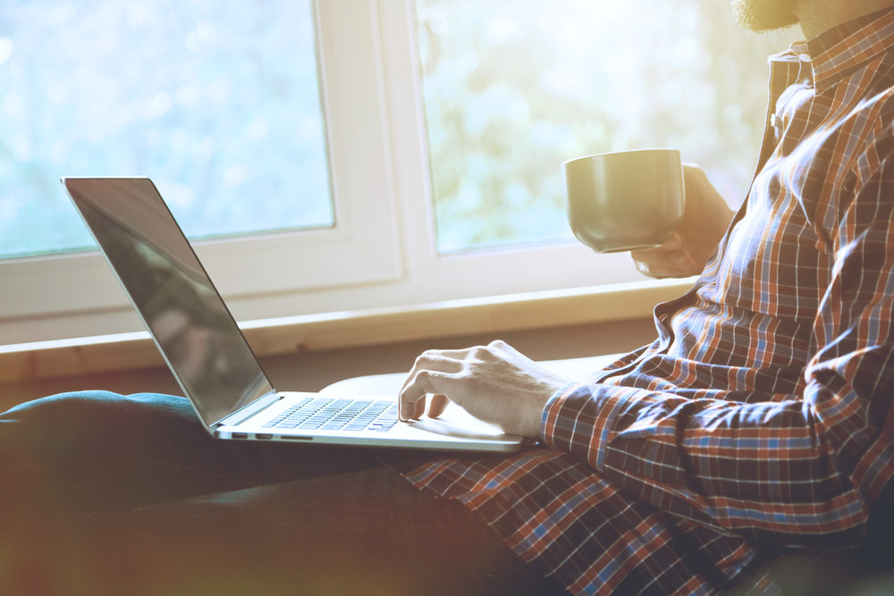 man lying with laptop drinking coffee