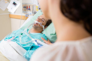 A male hospital patient with a breathing tube lies in bed