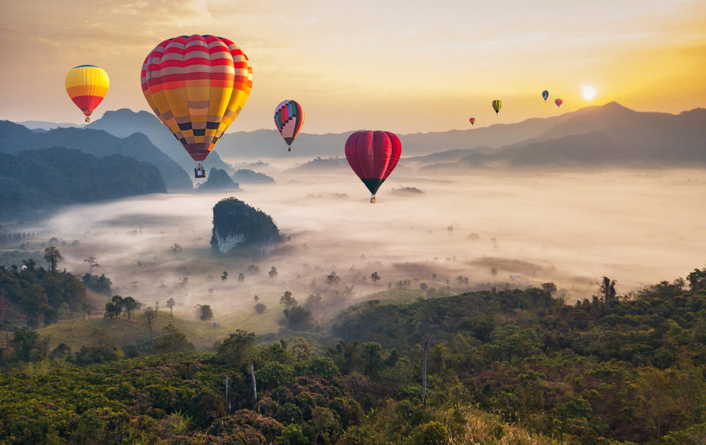 Colorful hot air balloons float above a misty tropical forest and mountains