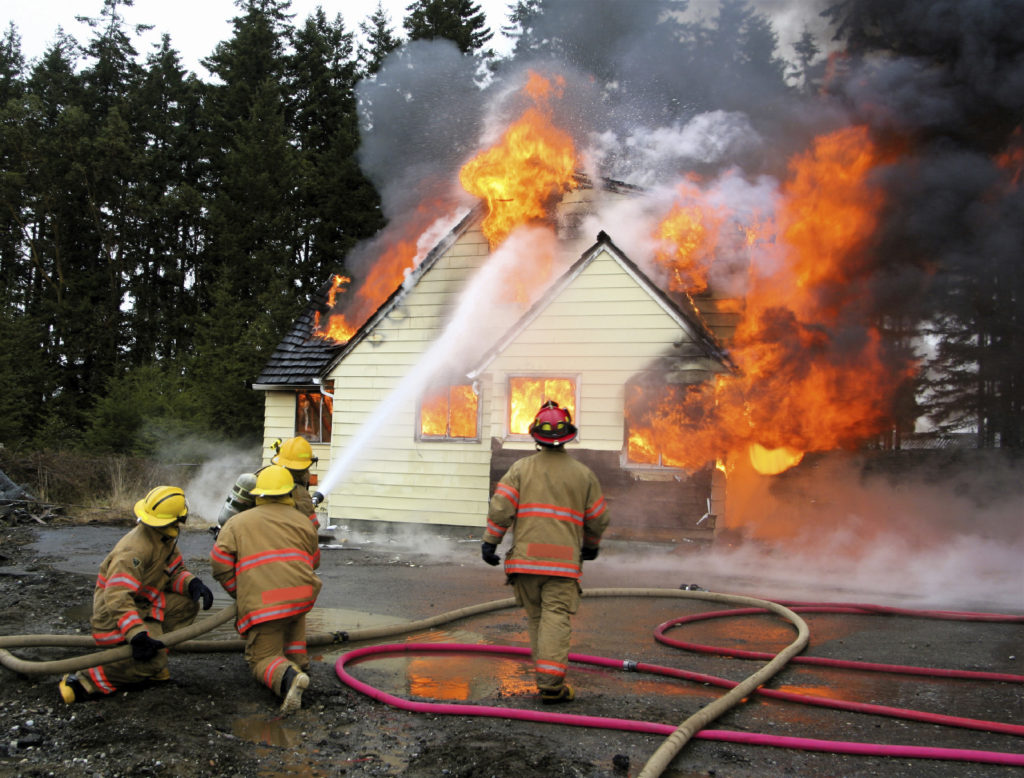 Several firefighters spraying water on a house engulfed in flames