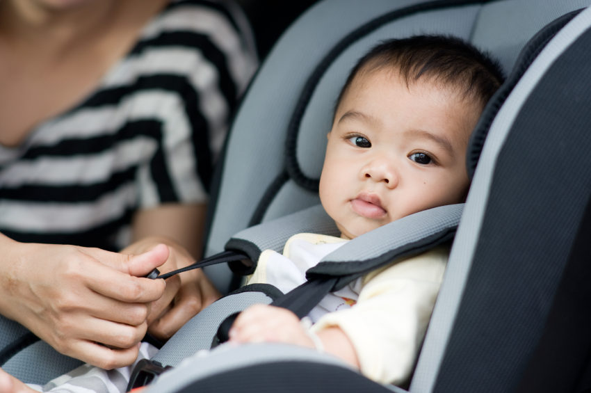 An infant strapped into a booster seat looks at the camera