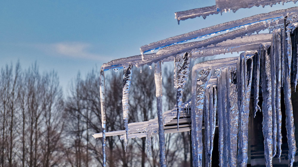 The shiny dangerous icicles hanging from the roof of a building against the sky