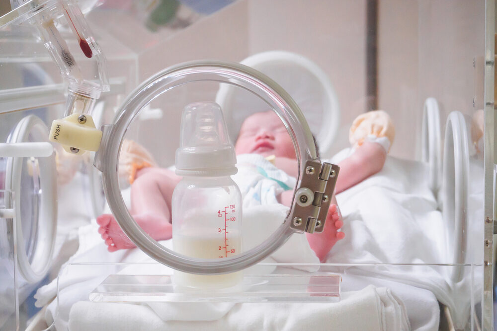 Do I Need To Hire An NEC Baby Formula Lawyer? Newborn baby girl inside incubator in hospital post delivery room with formula bottle