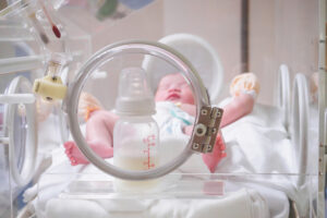 Newborn baby girl inside incubator in hospital post delivery room with formula bottle