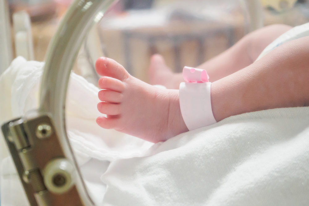Newborn girl baby inside incubator in hospital post delivery room with identification bracelet