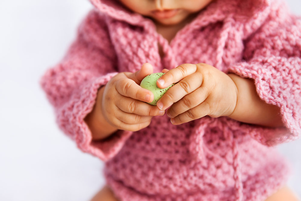 Little baby girl in pink romper playing with green Easter egg 