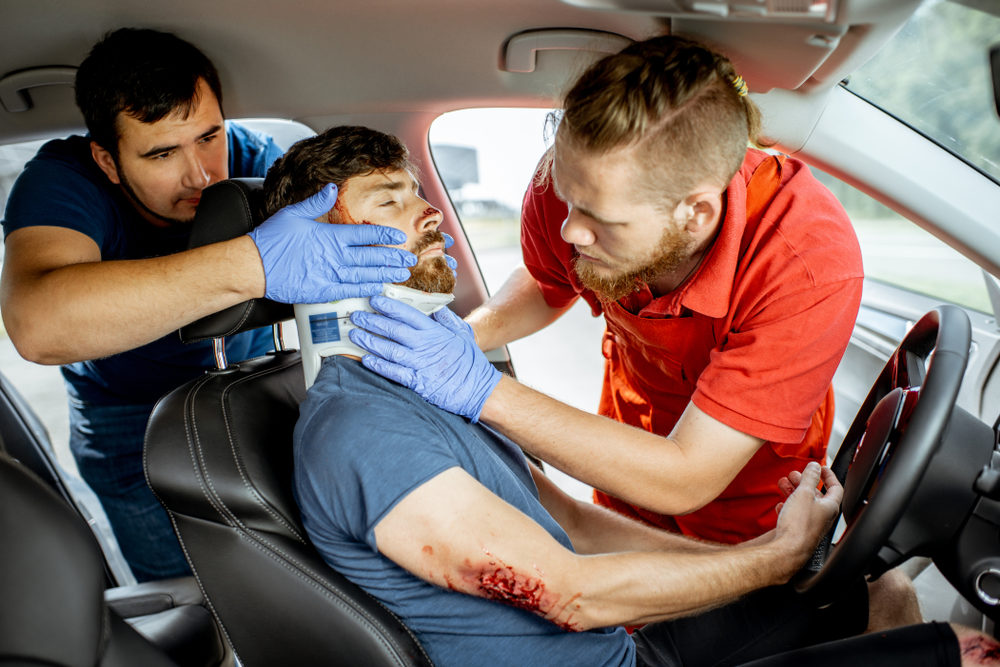 Medics wearing neck corset to an injured man sitting in the car after the road accident, providing emergency medical assistance