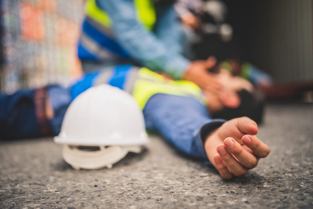 WMT Worker Dies After Stepping on an Unsecured Beam in Lakewood Construction Accident blurred image of an injured worker lying on the ground next to a hardhat with coworker checking on him