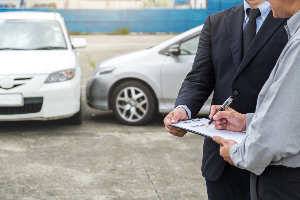 Insurance Agent examine Damaged Car and customer filing signature on Report Claim Form process after accident