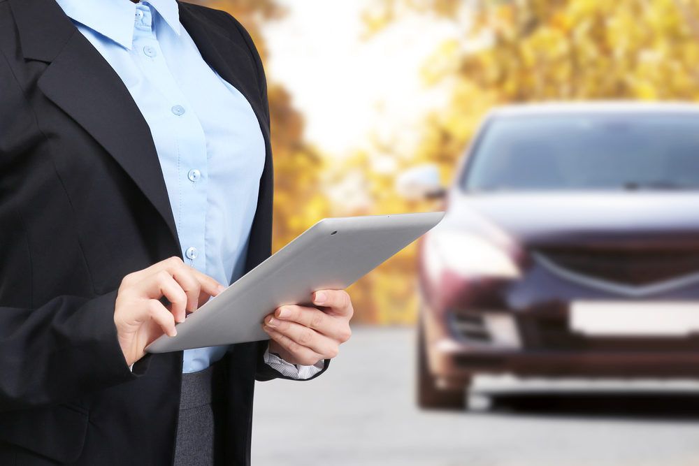 Insurance agent using tablet in front of car 