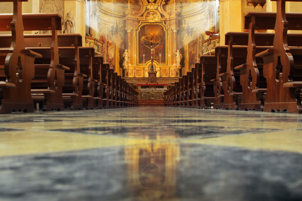 Interior of a beautiful old catholic church from below with marble floor, wooden pews, and light streaming onto altar with Jesus on crucifix