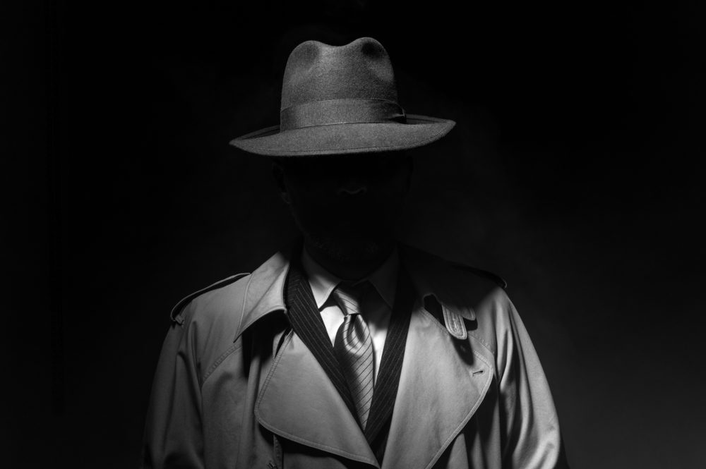 A well dressed man in a fedora, his face completely hidden in shadow