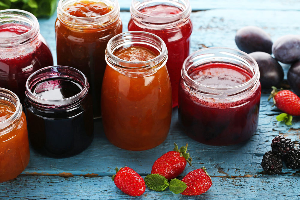 Glass jars with different kinds of jam and berries on wooden table