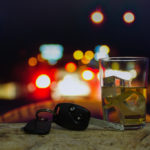 keys and an alcoholic beverage with car lights in background