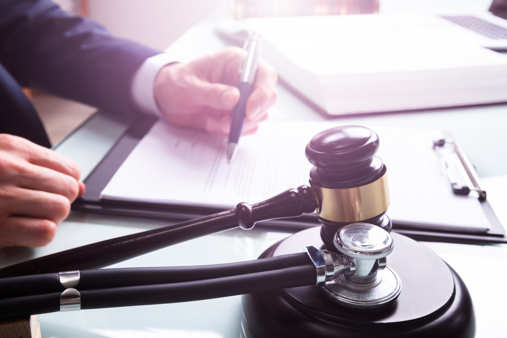 Attorney Writing On Legal Documents With Mallet And Stethoscope 