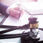 Attorney Writing On Legal Documents With Mallet And Stethoscope 