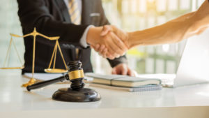 male lawyer shaking hands with client across desk with gavel laptop and scales of justice