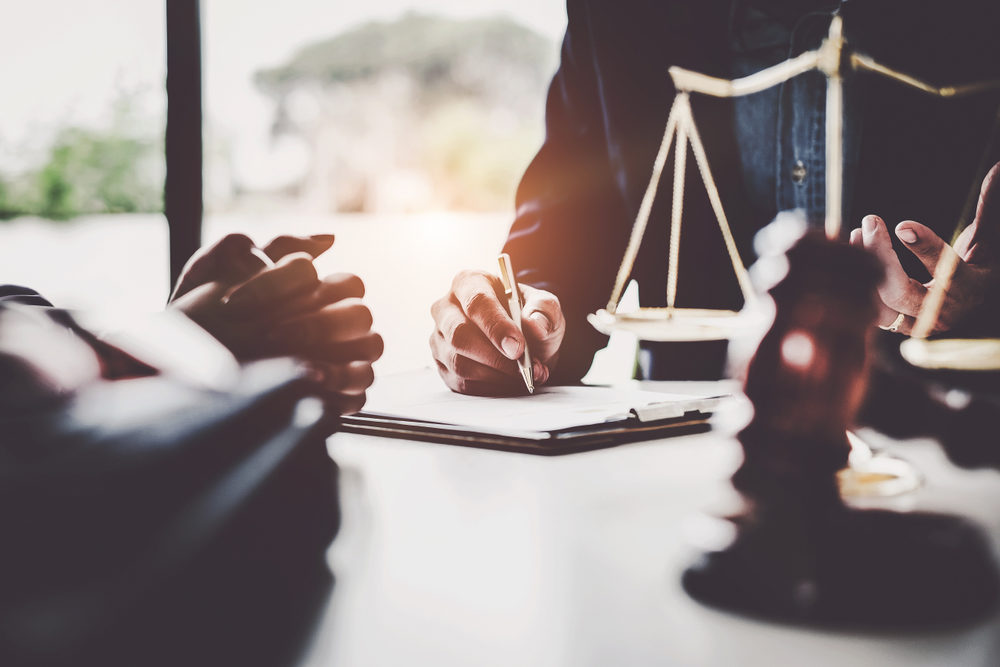 lawyers discussing contract papers with brass scale on wooden desk in office.