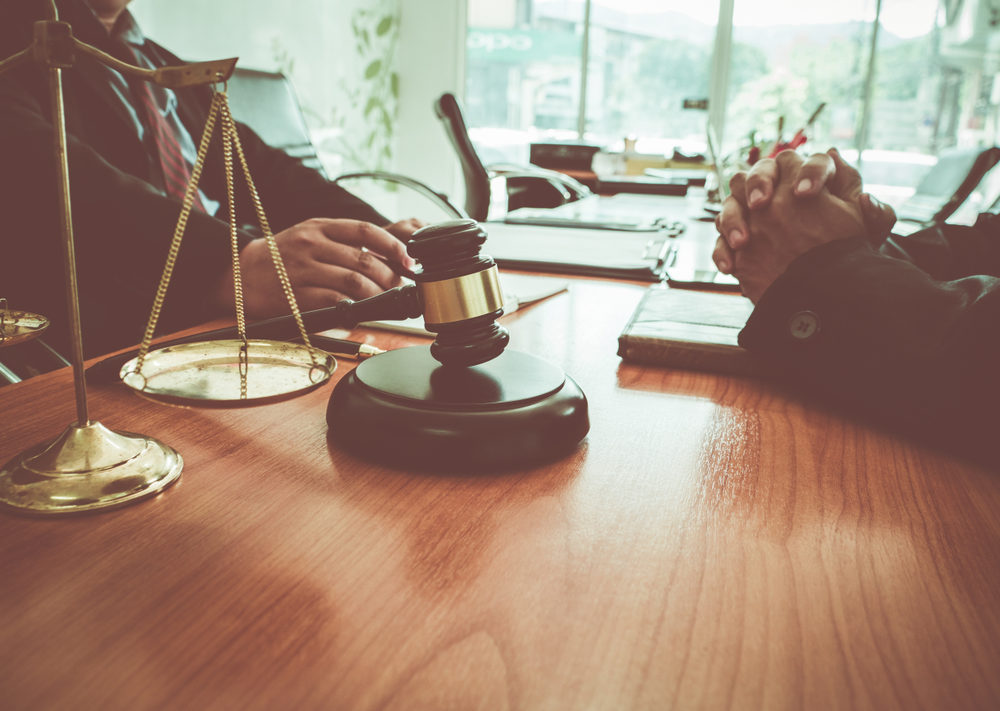 Lawyer providing counsel to client at desk with gavel and scales in forefront