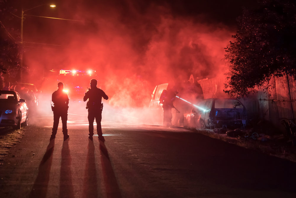 Firefighters and police officers extinguish a vehicle fire in the middle of the night.