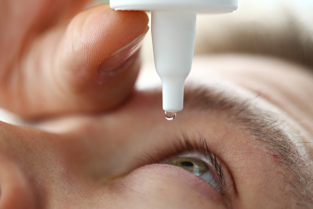 Male hand putting liquid drops in his eye solving vision problem closeup