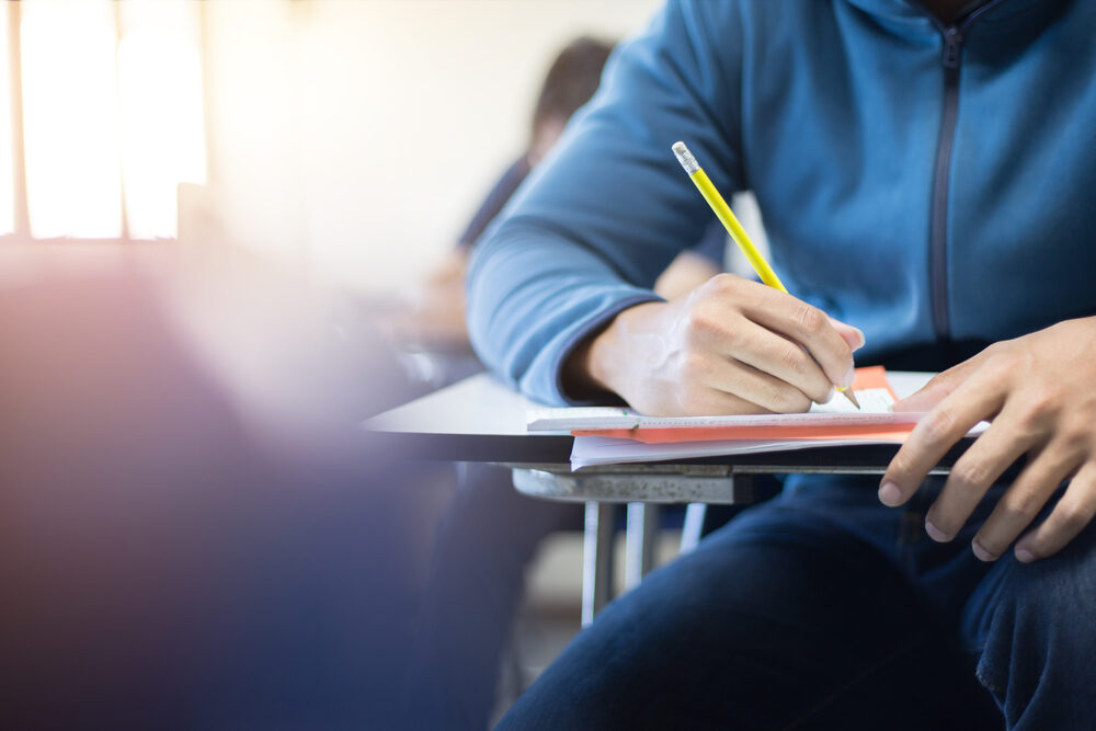 male student completing an exam at desk in school