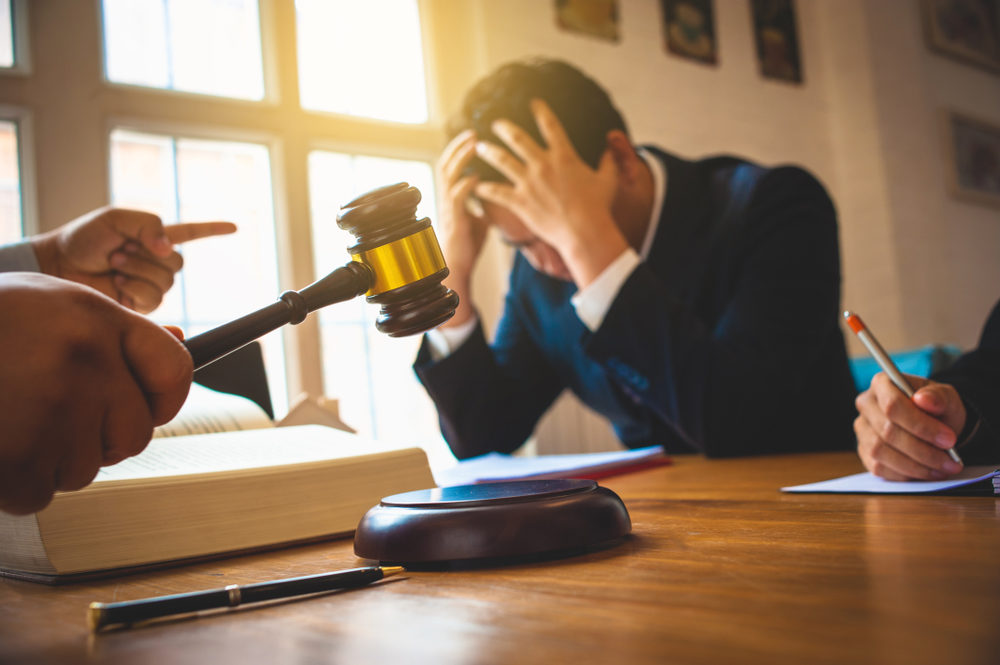 Man holding his head in his hands as a judge bangs a gavel