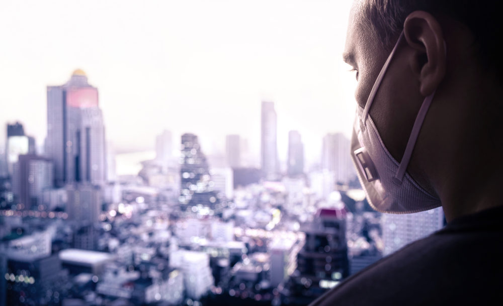 A man wears a face mask as he overlooks a large urban district from above