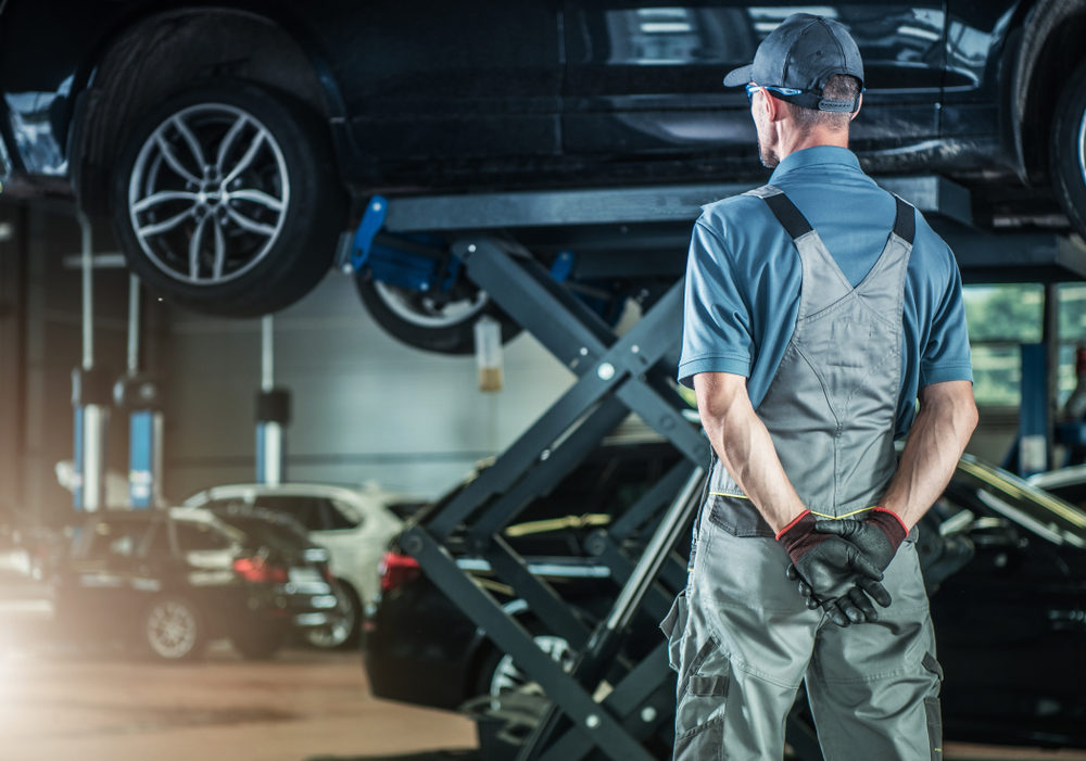 caucasian male mechanic observing a vehicle on a lift in a auto garage