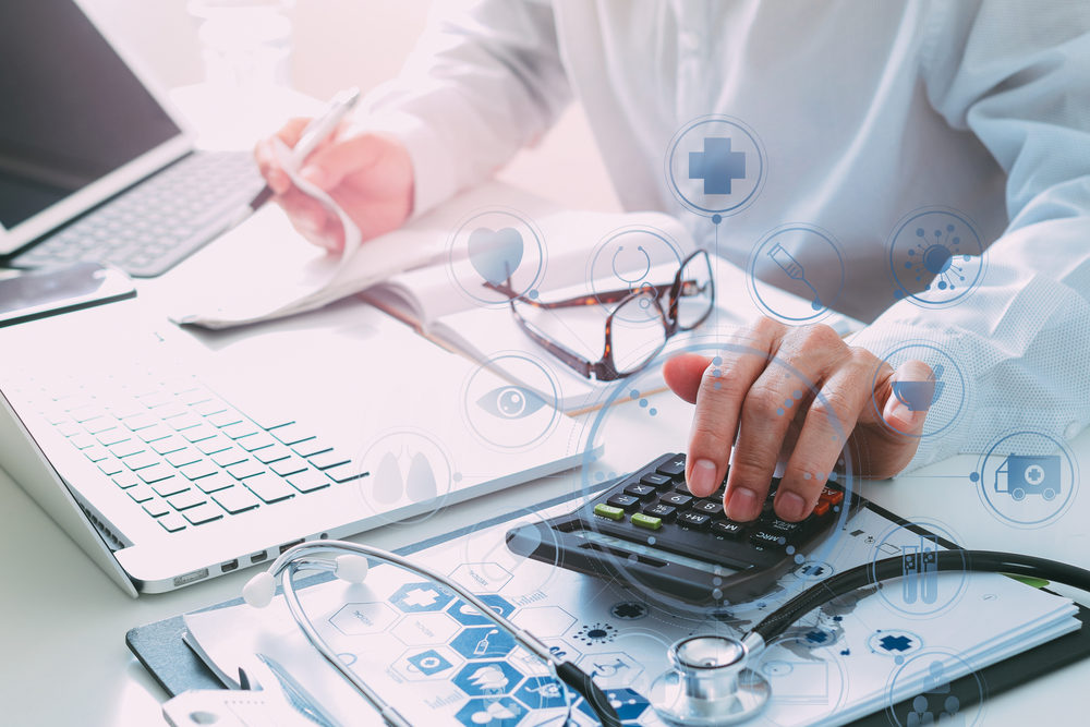doctor calculating medical costs with a calculator and laptops with healthcare icons