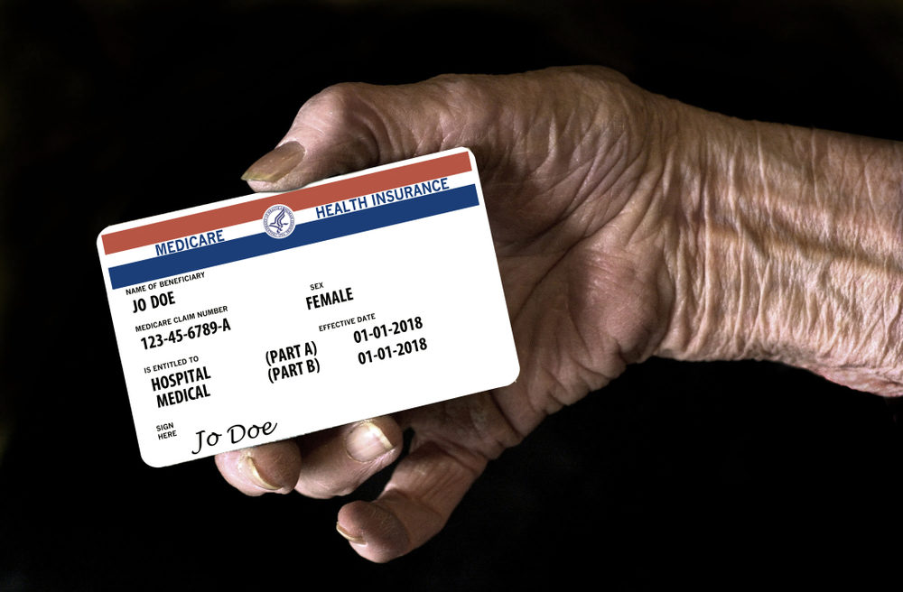 An elderly female hand holds a mock United State government Medicare Health Insurance card.