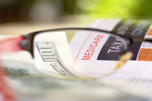 Medicare paper headline through reading glasses with hundred dollar bills
