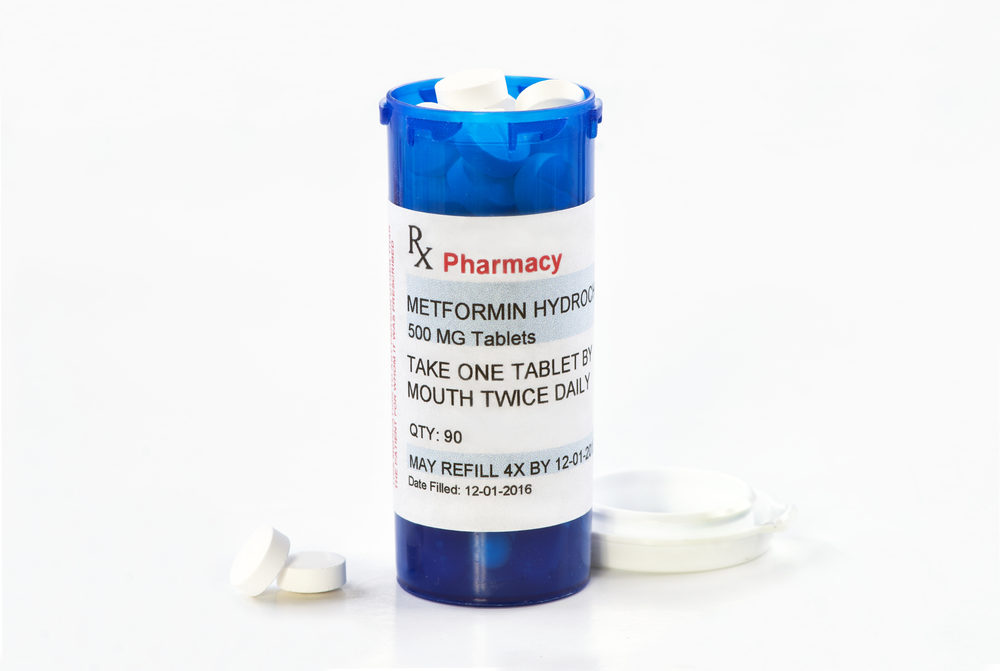 metformin bottle with lid removed and two tablets on white table with white background