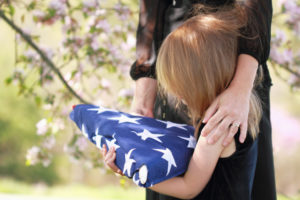 Daughter holding a parent's folded American flag with a woman's arms wrapped around her.
