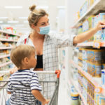 mother wearing prevention mask and her little son shopping for formula in a supermarket